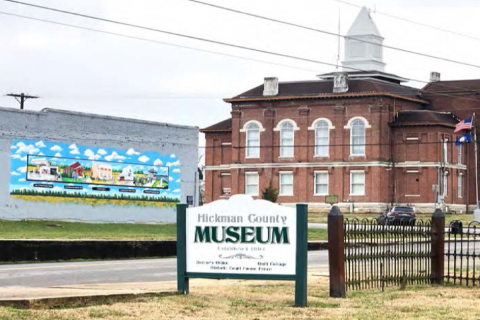 photograph of Hickman, KY showing a sign for the Hickman County Museum, Community Mural and their red brick downtown courthouse